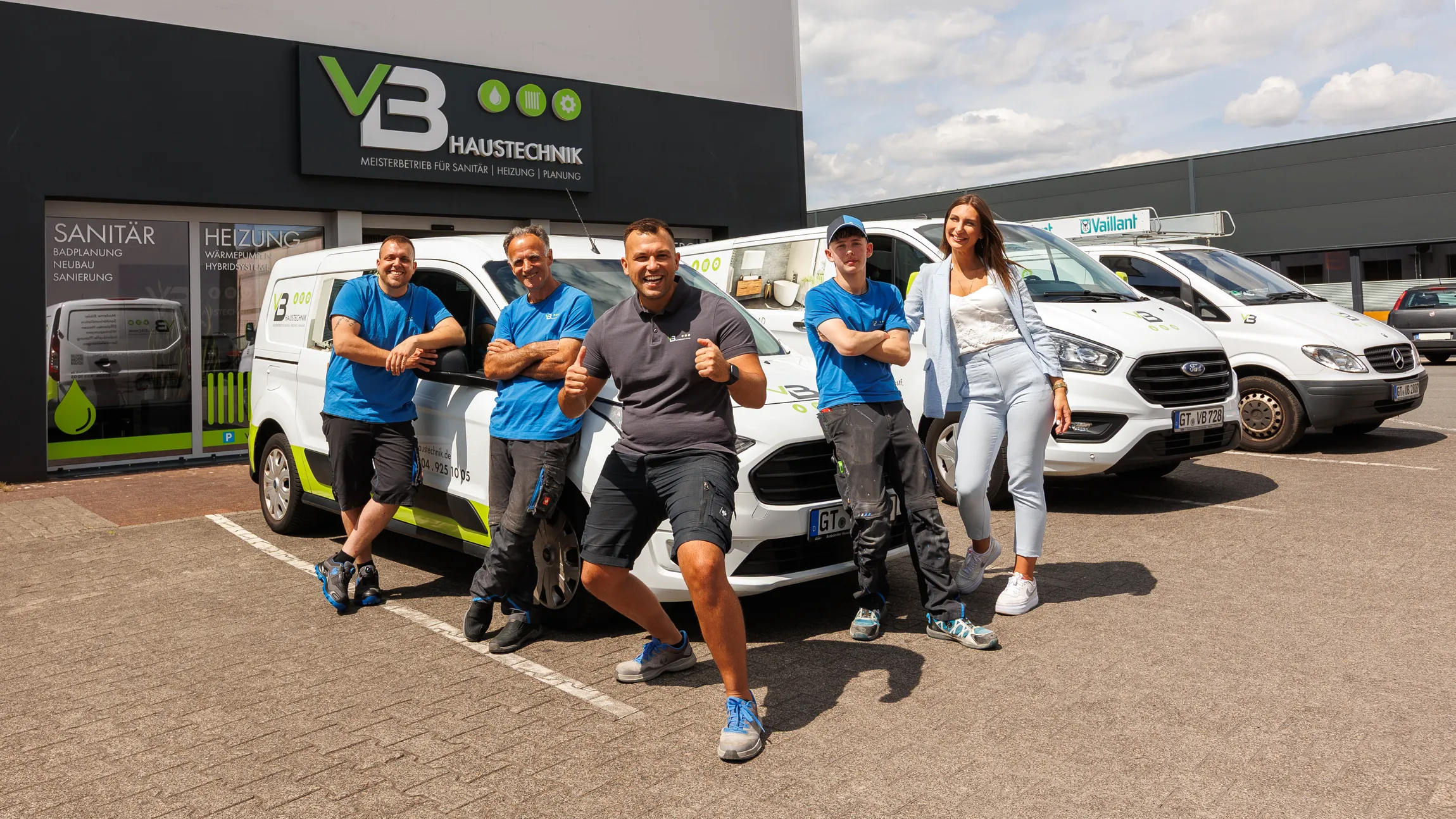 Team der VB Haustechnik steht vor den drei Werkstattfahrzeugen mit dem Firmengebäude im Hintergrund.
