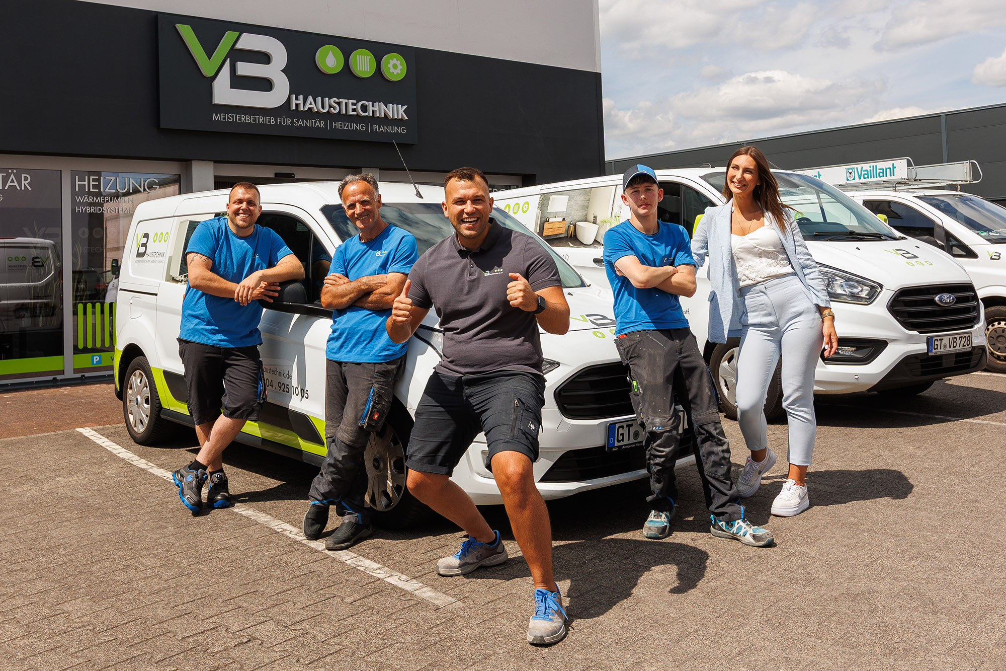 Team der VB Haustechnik steht vor den drei Werkstattfahrzeugen mit dem Firmengebäude im Hintergrund.